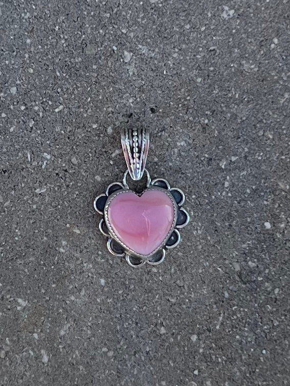 Pink heart-shaped pendant with silver frame on a gray surface